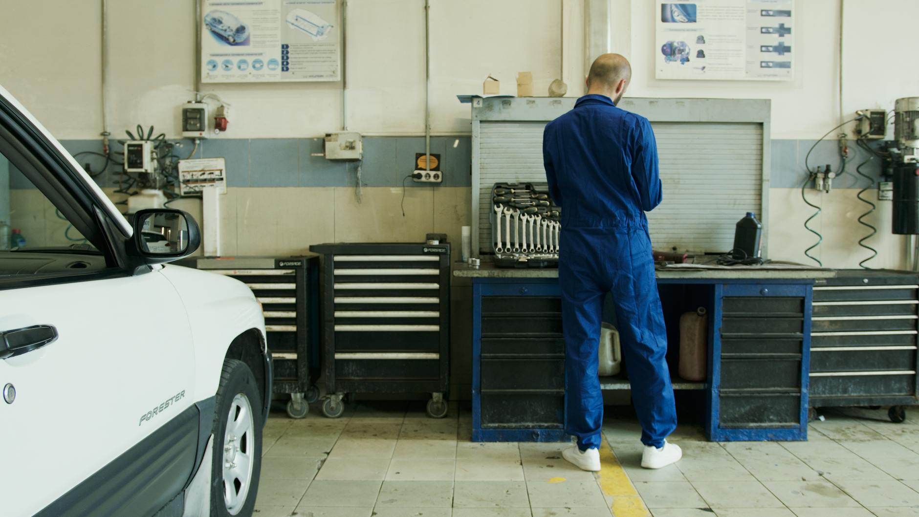 Mechanik w niebieskim kombinezonie sprawdza białe Volvo XC60 w warsztacie