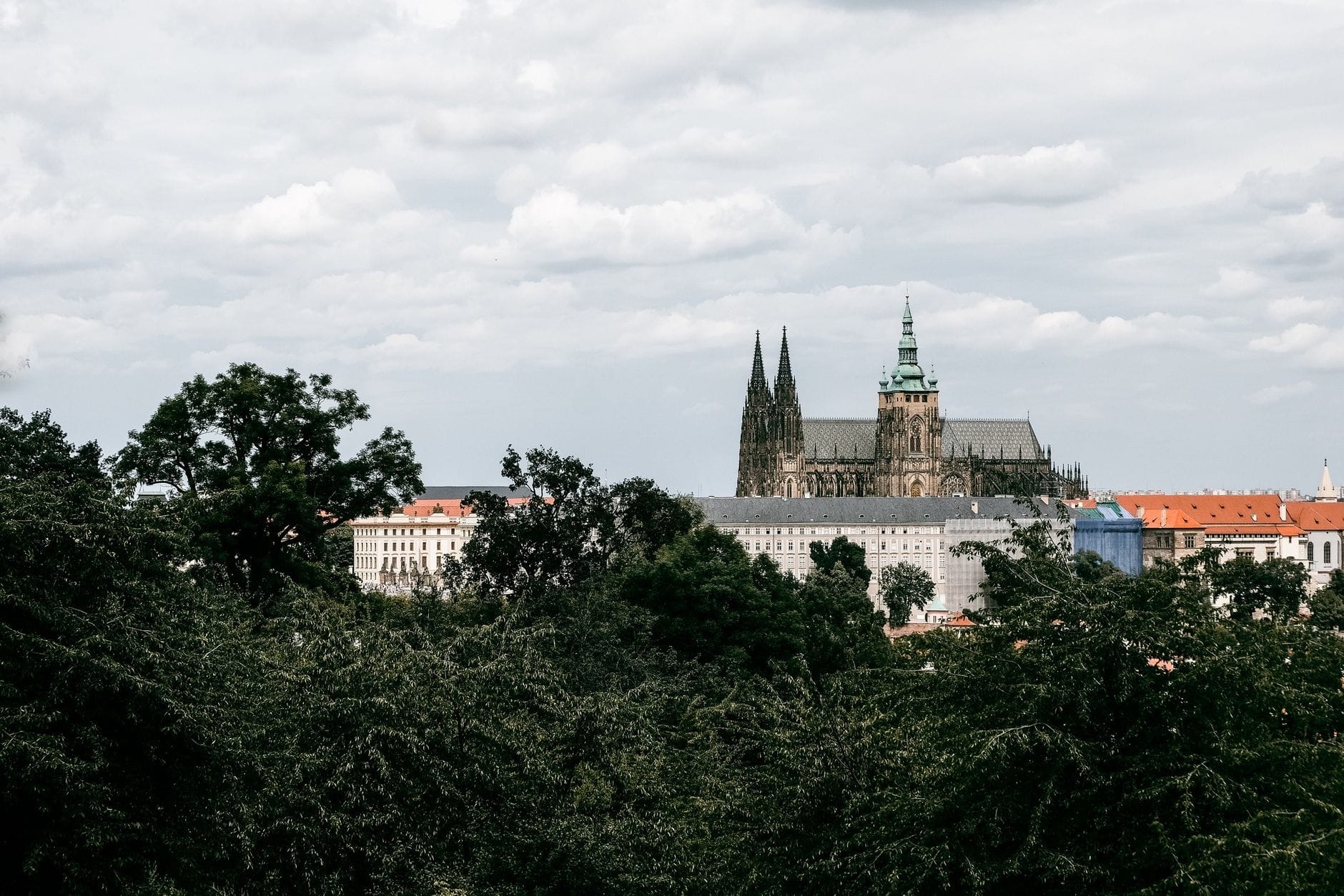 Panorama Zamku Praskiego otoczonego zielenią pod pochmurnym niebem